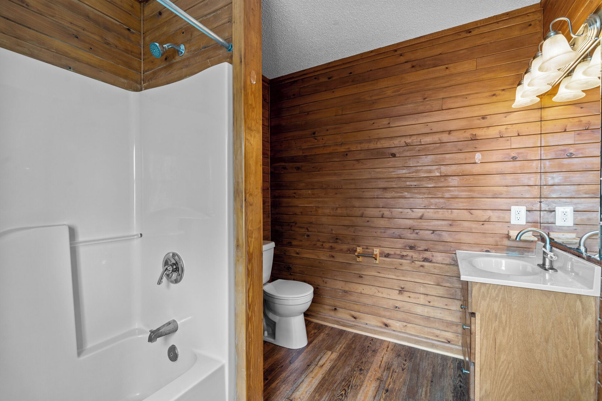 A bathroom with a wooden wall, a white bathtub, a toilet, and a sink with a mirror.