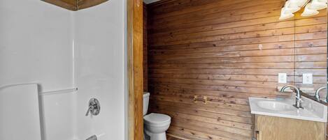 A bathroom with a wooden wall, a white bathtub, a toilet, and a sink with a mirror.