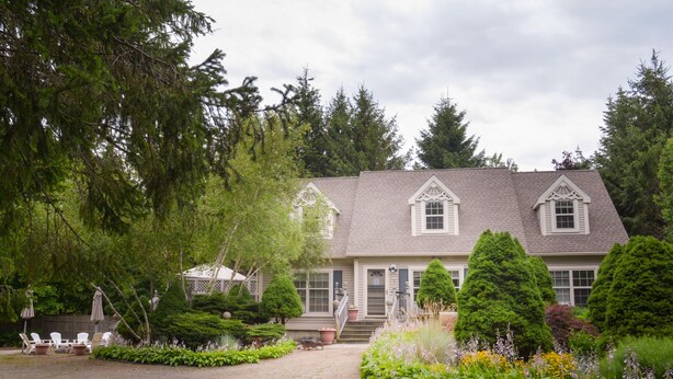 A two-story house with a symmetrical facade, a front porch, and a well-maintained garden with various plants and flowers. - Cozy Dog Friendly House with Deck, Firepit & Fast WiFi in Heart of Bar Harbor (Bar Harbor)