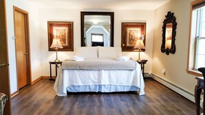 A bedroom with a large bed, two bedside lamps, a mirror, and a window. - Cozy Dog Friendly House with Deck, Firepit & Fast WiFi in Heart of Bar Harbor (Bar Harbor)