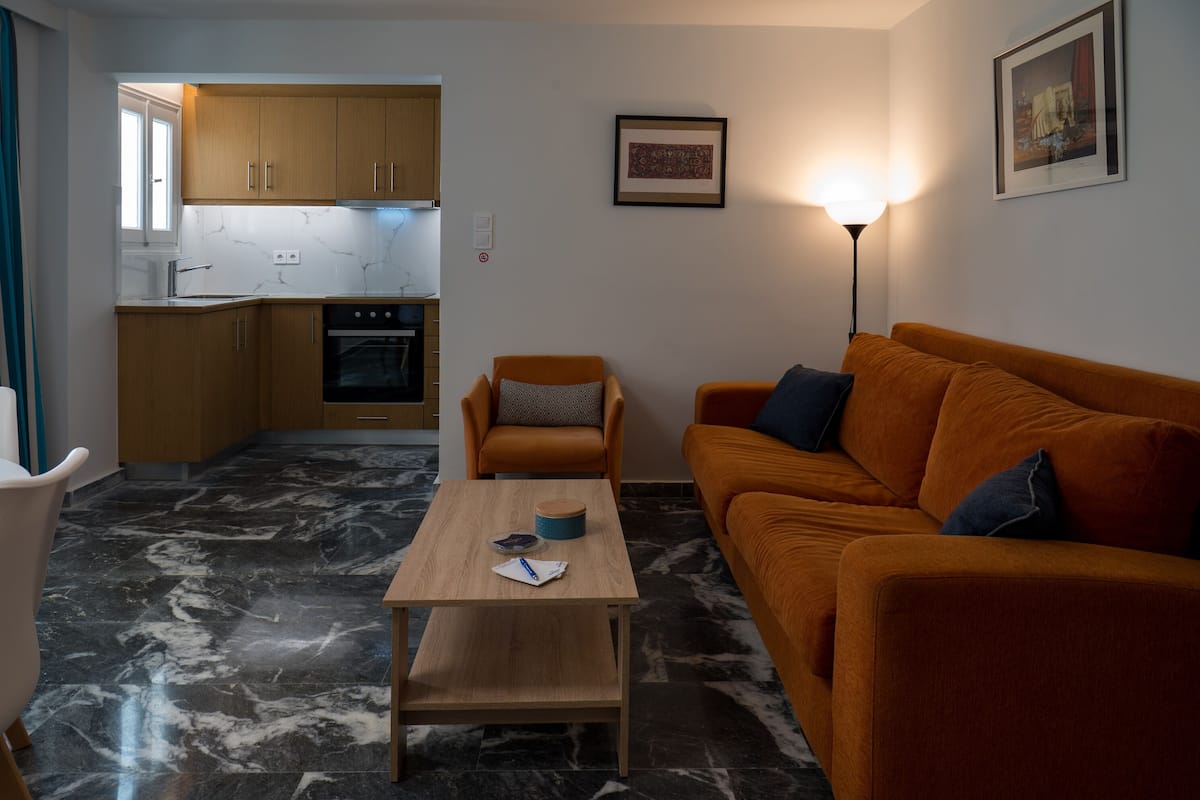 A compact living space with a kitchen, a wooden table, an orange sofa, and a floor with a marble pattern.