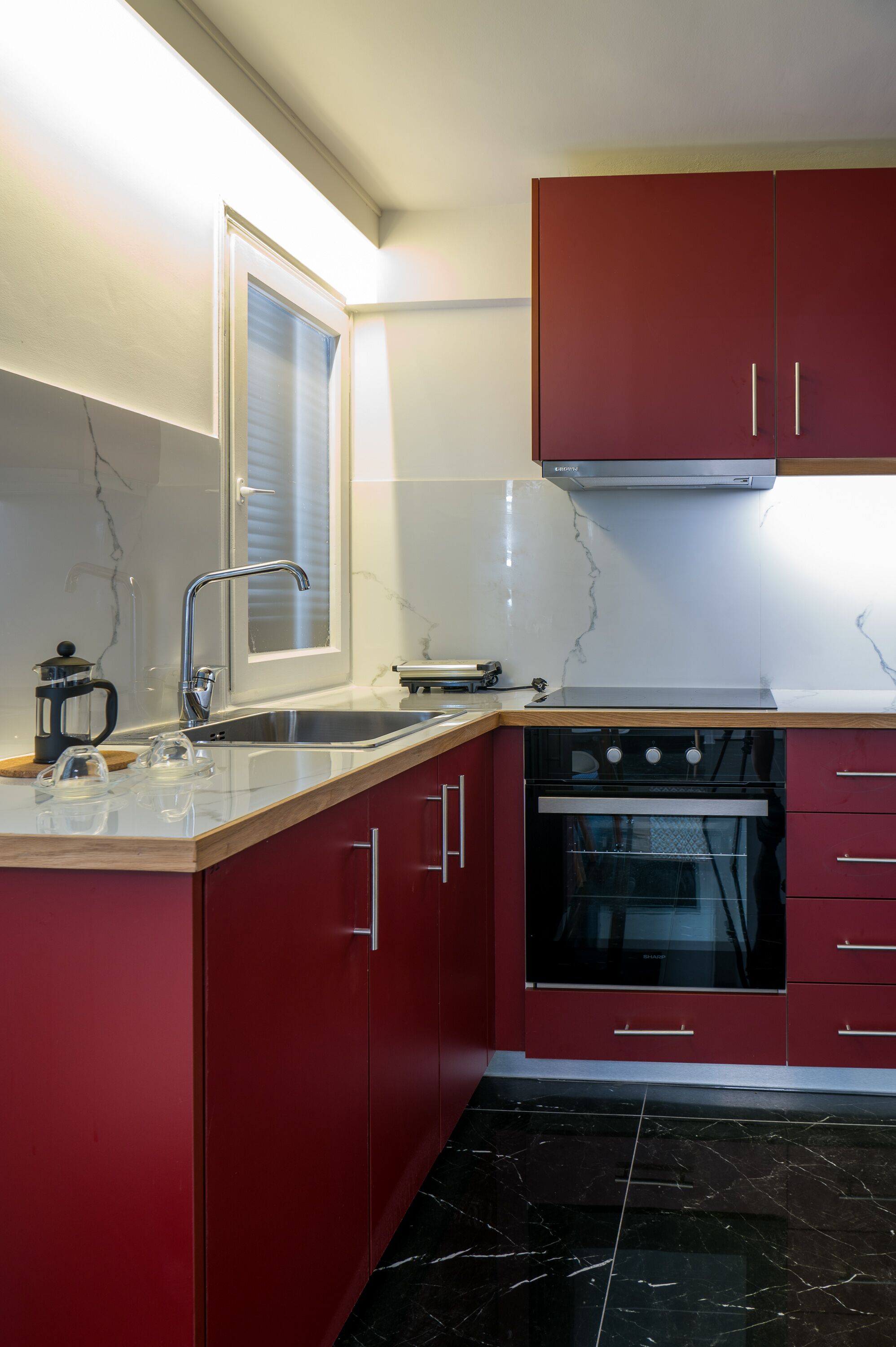 Una cocina moderna con armarios rojos, un lavamanos de acero inoxidable y un horno negro.