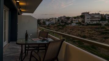 A balcony with a table and chairs, overlooking a residential area with buildings and a hilly landscape.