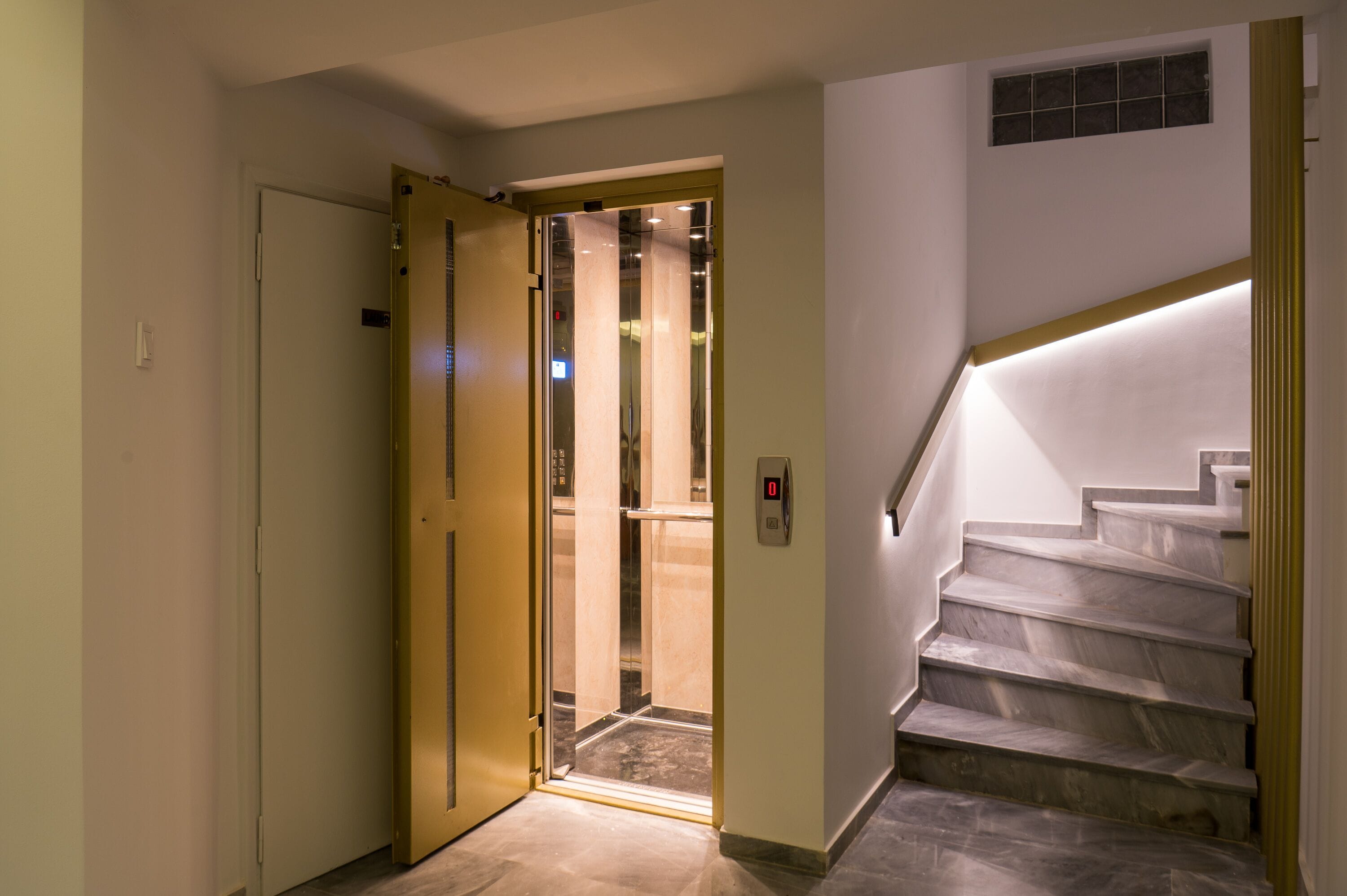 Een hotelhal met een marmeren trap, een deur naar een kamer en een verlichte muur.