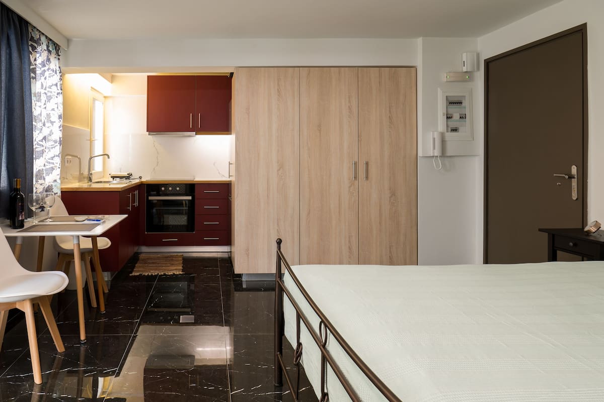 A hotel room with a bed, a small kitchenette, a dining area, and a bathroom.