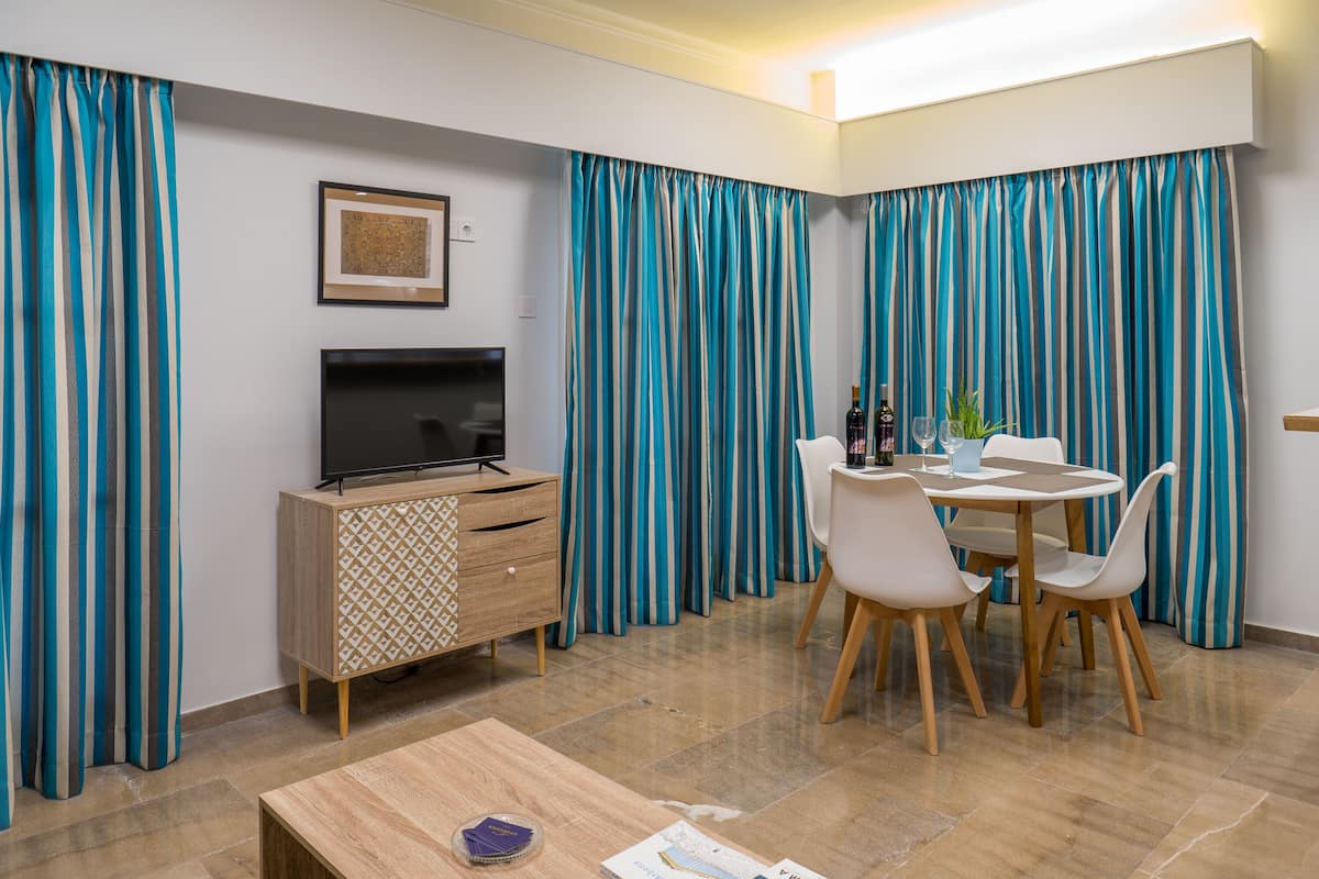 A modern living room with a TV, wooden cabinet, dining table, chairs, and striped curtains.