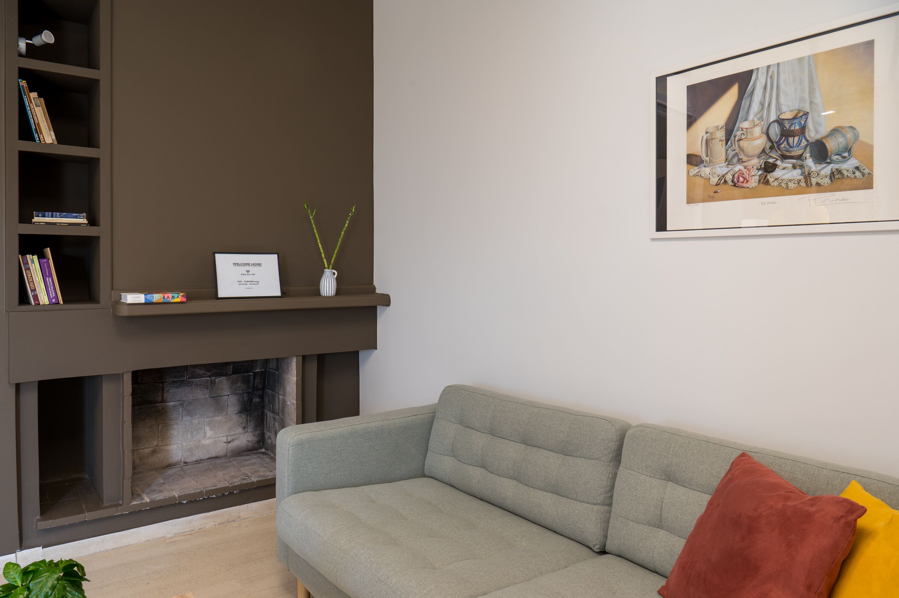 A living room with a grey sofa, a fireplace, a bookshelf, and a framed artwork on the wall.