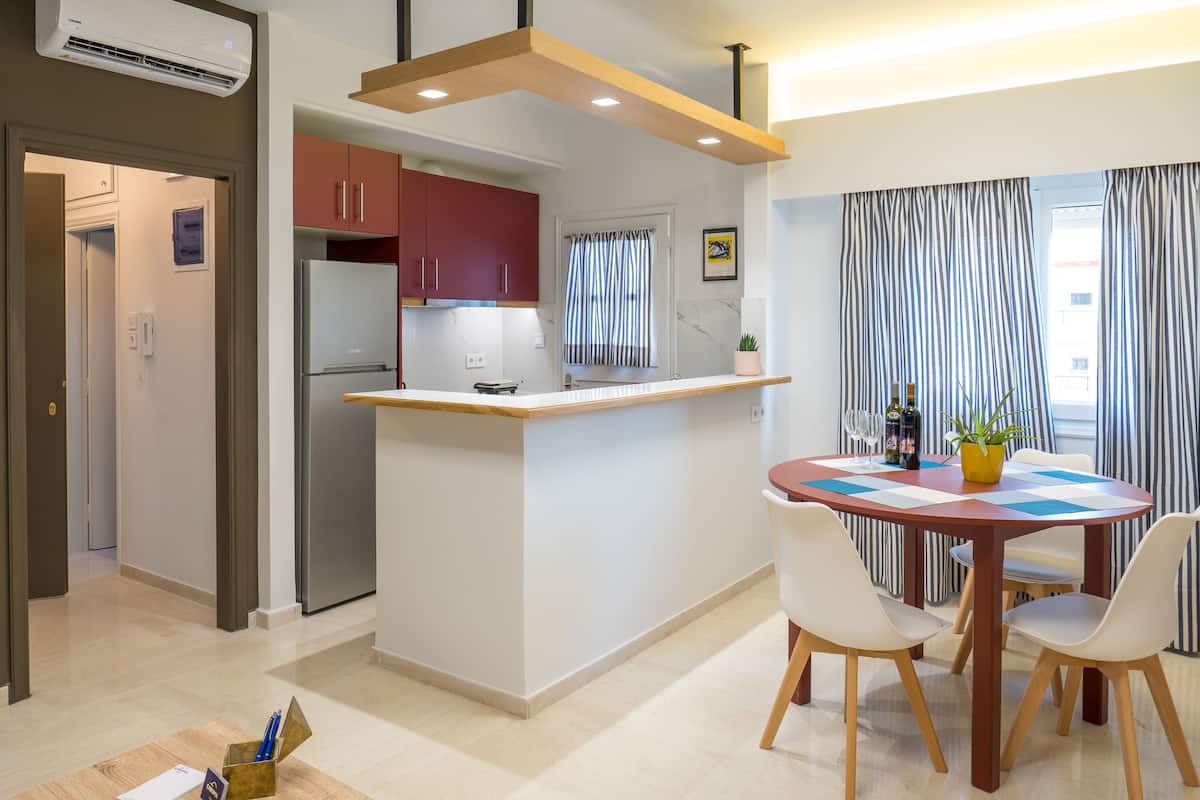 A modern kitchen with a central island, a dining area with a checkered table, and striped curtains.