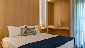 A hotel room with a large bed, a nightstand with a lamp, a wooden wardrobe, and a small statue on the wardrobe. - CHROMA Lodge Rafina (Rafina-Pikermi)