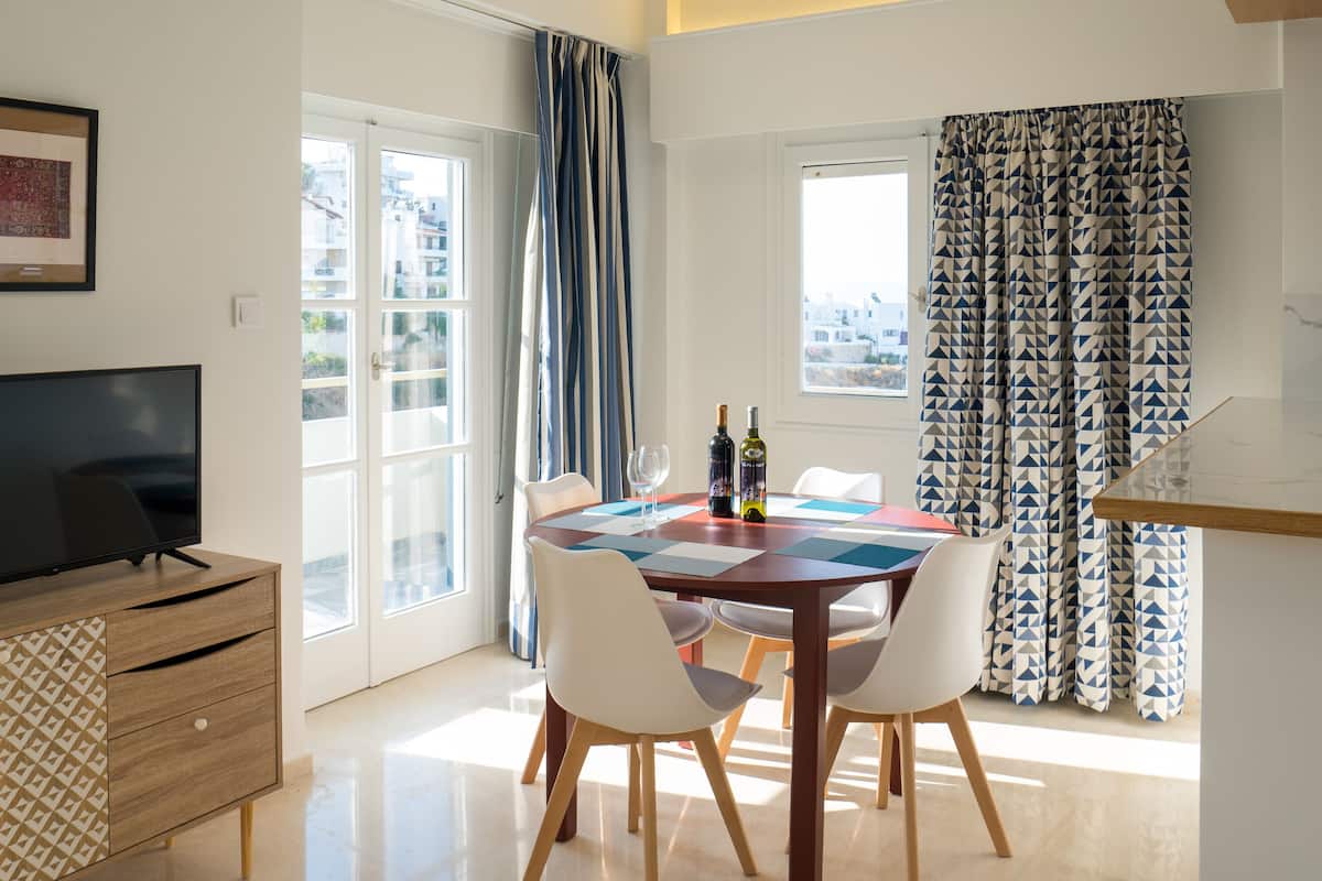 A dining area with a table set for four, a television on a wooden cabinet, and a city view through the windows.