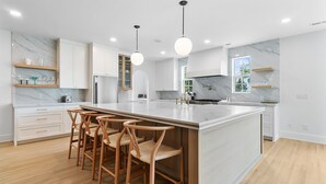 A modern kitchen with a large island, wooden bar stools, white cabinetry, and pendant lighting. - THE PEARL!  7bd/7ba IOP Home Private POOL & Ocean VIEWS! (Isle Of Palms)