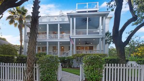 A two-story white building with balconies, a flag, and a pathway leading to the entrance. - THE PEARL!  7bd/7ba IOP Home Private POOL & Ocean VIEWS! (Isle Of Palms)