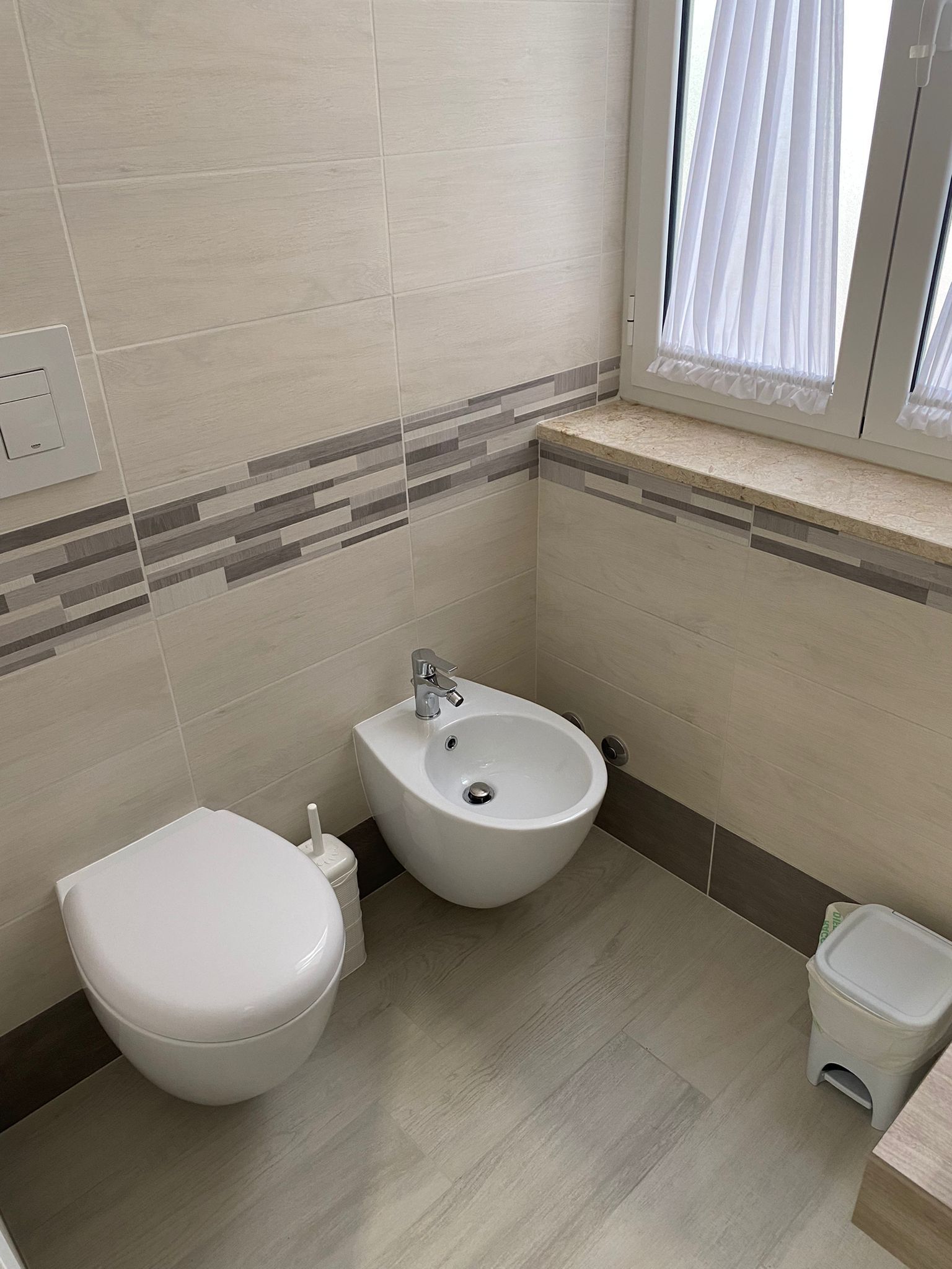 A small bathroom with a toilet, bidet, and a trash bin.