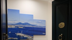 A hallway with a black door, a wall-mounted artwork depicting a coastal scene, and a plaque on the door. - Toledo Relax (Naples)