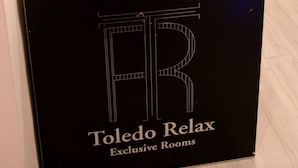 A reception desk with a framed collage of photos, a QR code, and a sign for "Toledo Relax Exclusive Rooms". - Toledo Relax (Naples)