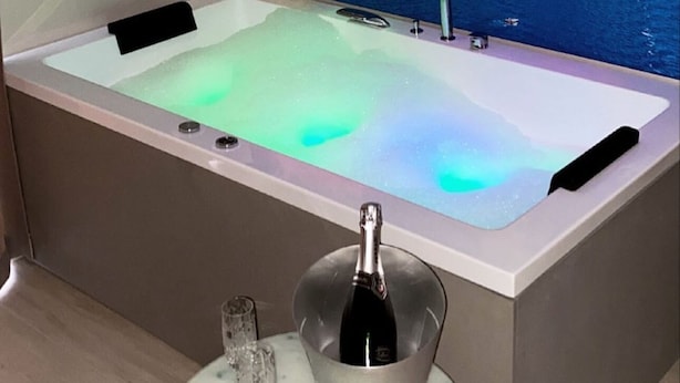 A modern bathroom with a large bathtub, a bottle of champagne, and a glass on a marble table. - Toledo Relax (Naples)