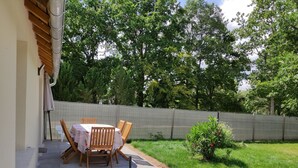An outdoor patio with a table and chairs, a small garden, and a fence. - A L'arborée de Clénord (Clénord-Cellettes)