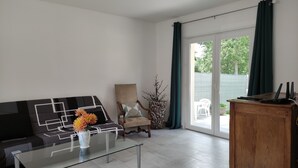 A modern living room with a glass coffee table, a sofa with patterned cushions, a wooden cabinet, and a chair with a patterned cushion. - A L'arborée de Clénord (Clénord-Cellettes)