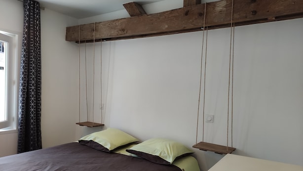 A bedroom with a bed, pillows, a wooden headboard, and a window with curtains. - A L'arborée de Clénord (Clénord-Cellettes)