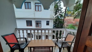Un balcon avec une table en bois et deux chaises, un bâtiment blanc en arrière-plan et une vue sur un arbre.