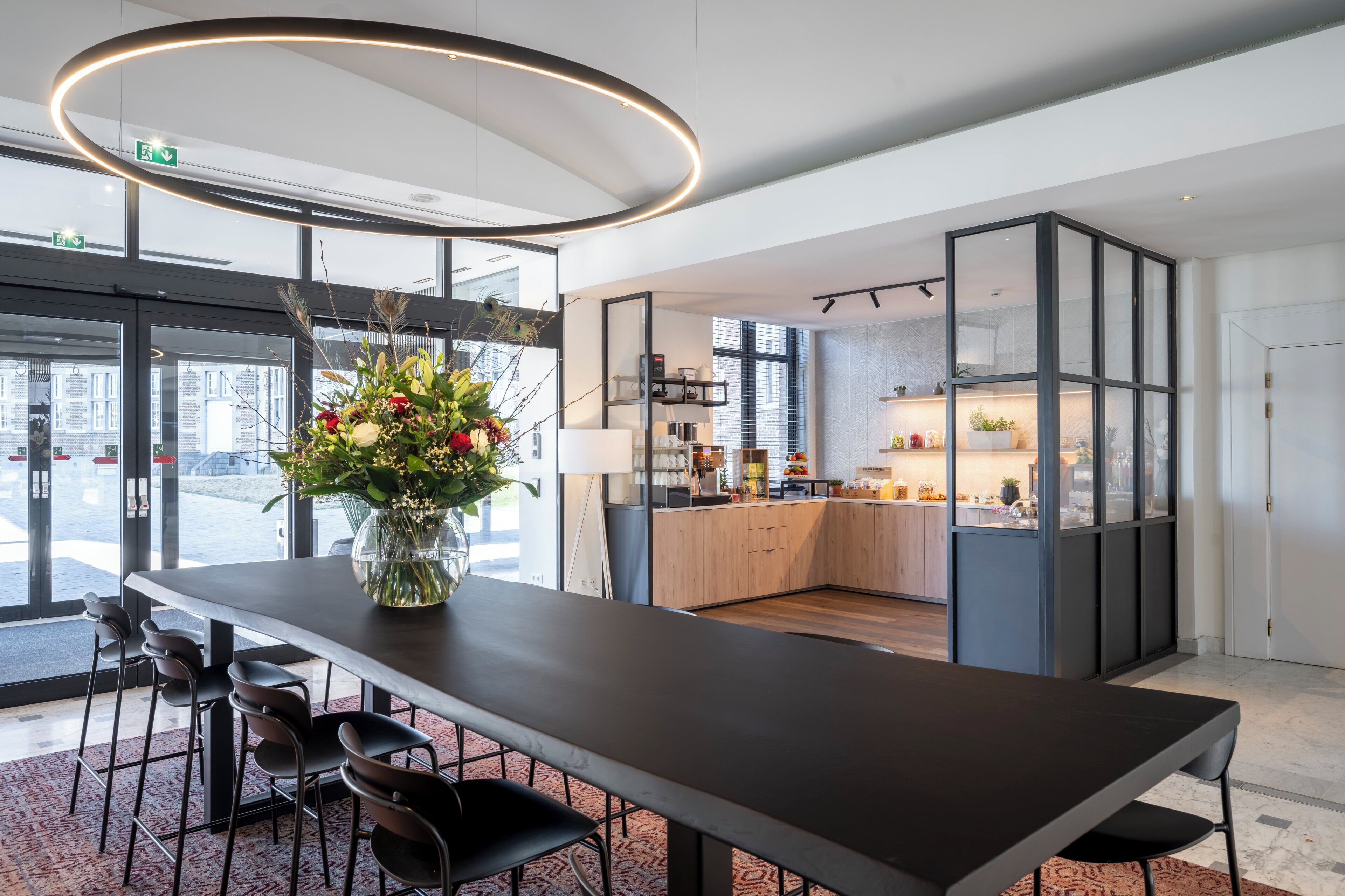 Een moderne eetruimte met een lange tafel, stoelen, een vaas met bloemen en een keuken op de achtergrond.