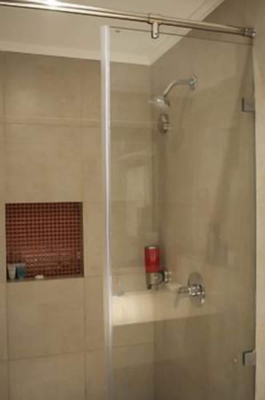 A glass-enclosed shower stall with a showerhead and a small shelf with toiletries.