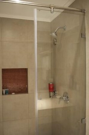 A glass-enclosed shower stall with a showerhead and a small shelf with toiletries. - Prideinn Paradise Beach Resort & Spa Mombasa (Mombasa)