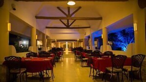 Comedor de hotel con mesas y sillas, un techo alto con vigas de madera y un amplio ventanal con vistas.