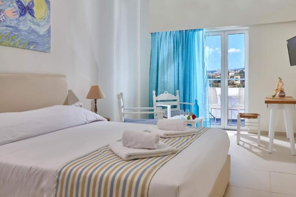 A hotel room with a bed, a chair, a table, and a view of the outside.