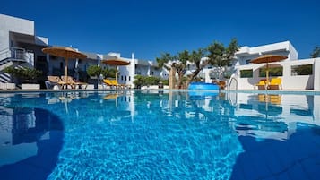 A swimming pool with lounge chairs and umbrellas, surrounded by white buildings.