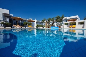 A swimming pool with lounge chairs and umbrellas, surrounded by white buildings. - Vasia Ormos Hotel (Agios Nikolaos)