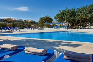 A pool area with lounge chairs and umbrellas, surrounded by trees and a clear sky.