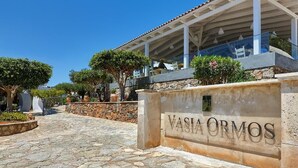 Un chemin de pierre mène à un bâtiment sur lequel on peut lire l’inscription suivante : « Vasia Ormos ».