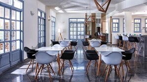 A spacious dining area with multiple tables and chairs, large windows, and a modern chandelier. - Vasia Ormos Hotel (Agios Nikolaos)
