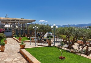 A courtyard with a stone building, potted plants, and a view of the landscape. - Vasia Ormos Hotel (Agios Nikolaos)