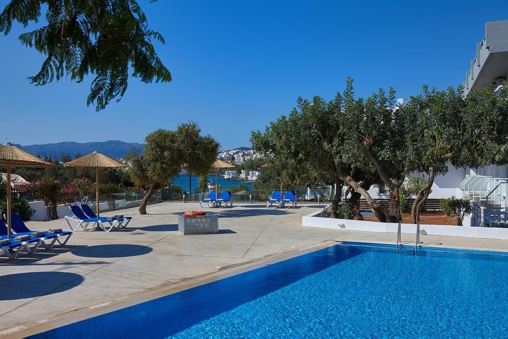A pool area with lounge chairs, umbrellas, and trees.