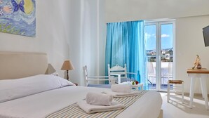 A hotel room with a bed, a chair, a table, and a view of the outside. - Vasia Ormos Hotel (Agios Nikolaos)