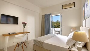 A hotel room with a bed, a desk, a chair, a TV, a window with curtains, and a balcony. - Vasia Ormos Hotel (Agios Nikolaos)
