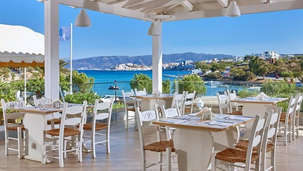 Un restaurant en bord de mer, doté d’une terrasse, de mobilier blanc et offrant une vue sur la mer et les bâtiments environnants.
