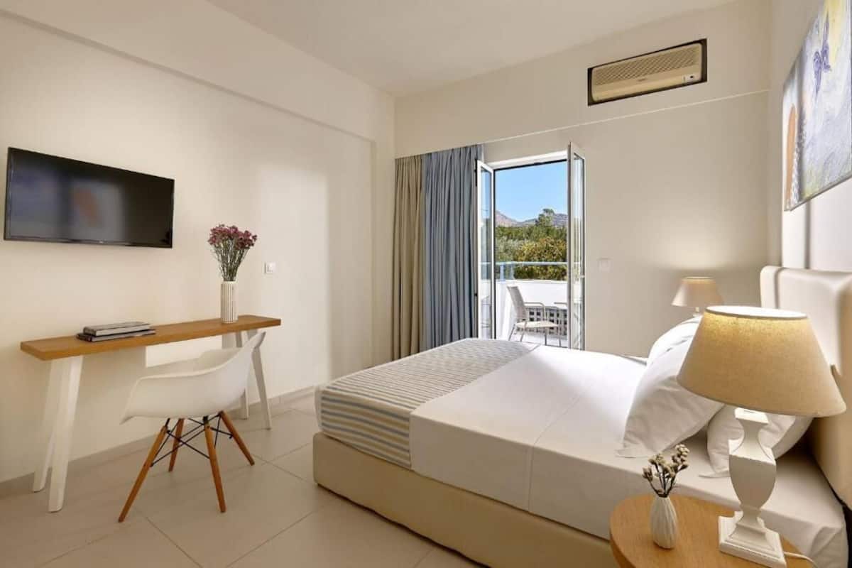 A hotel room with a bed, a desk, a chair, a TV, a window with curtains, and a balcony.