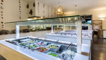 A buffet area with multiple food stations, a glass partition, and a chef preparing food.