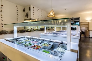 A buffet area with multiple food stations, a glass partition, and a chef preparing food. - Vasia Ormos Hotel (Agios Nikolaos)