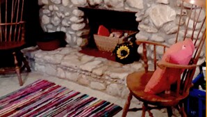 Une cheminée en pierre, un tapis aux couleurs vives et deux chaises en bois.