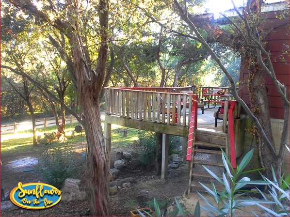 A wooden bridge with a red railing leading to a red building, surrounded by trees and greenery.