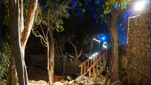Un espace extérieur aménagé pour la nuit, avec un mur en pierre, une rambarde en bois et un chemin menant à un bâtiment.