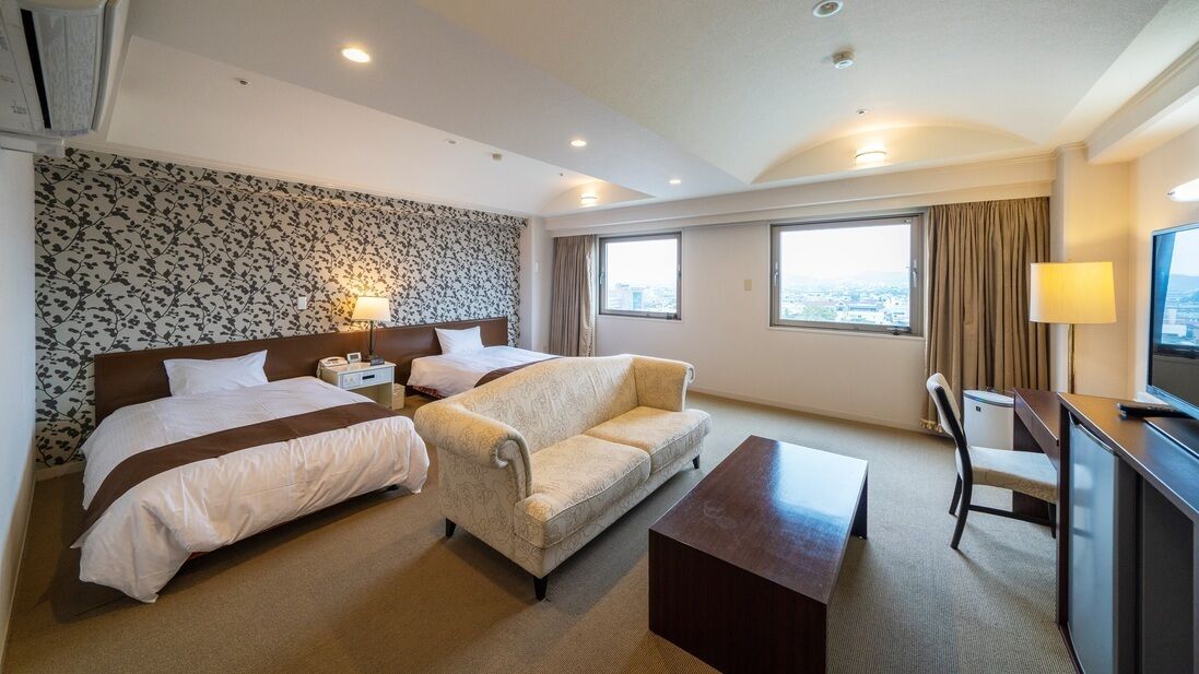 A hotel room with two beds, a sofa, a desk, and a TV.