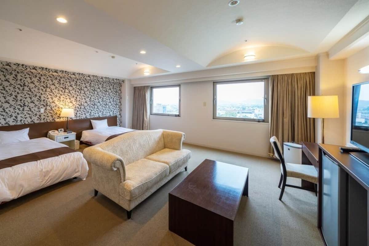 Habitación de hotel con dos camas, un sofá, un escritorio y una televisión.
