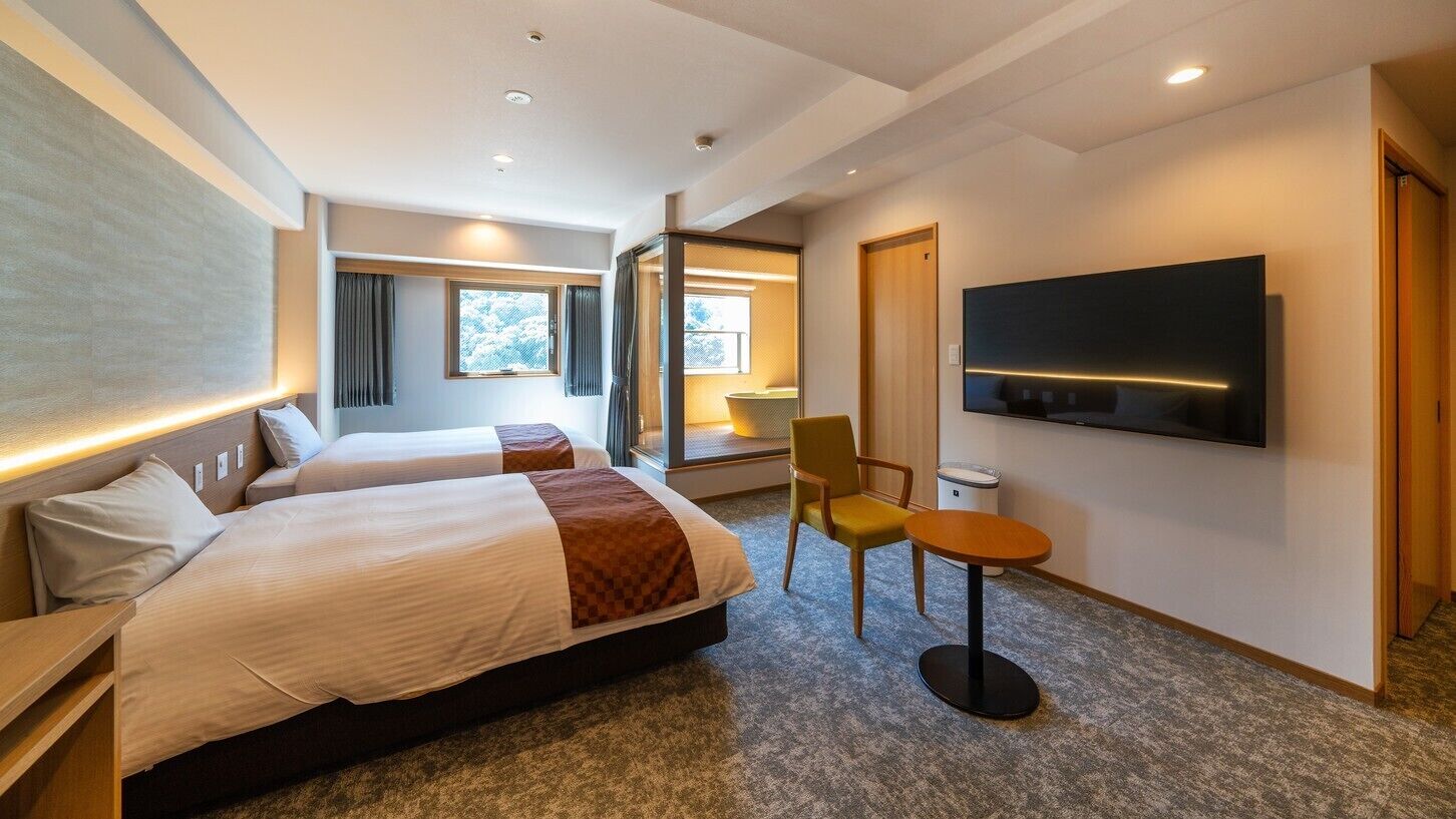 A hotel room with two beds, a TV, a small table, and a chair.