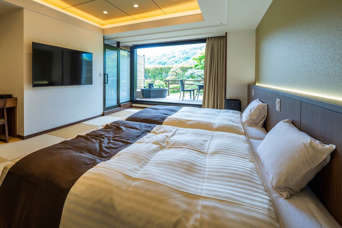Habitación de hotel con una cama grande, un escritorio con televisor de pantalla plana y vista a un jardín por una puerta corrediza.