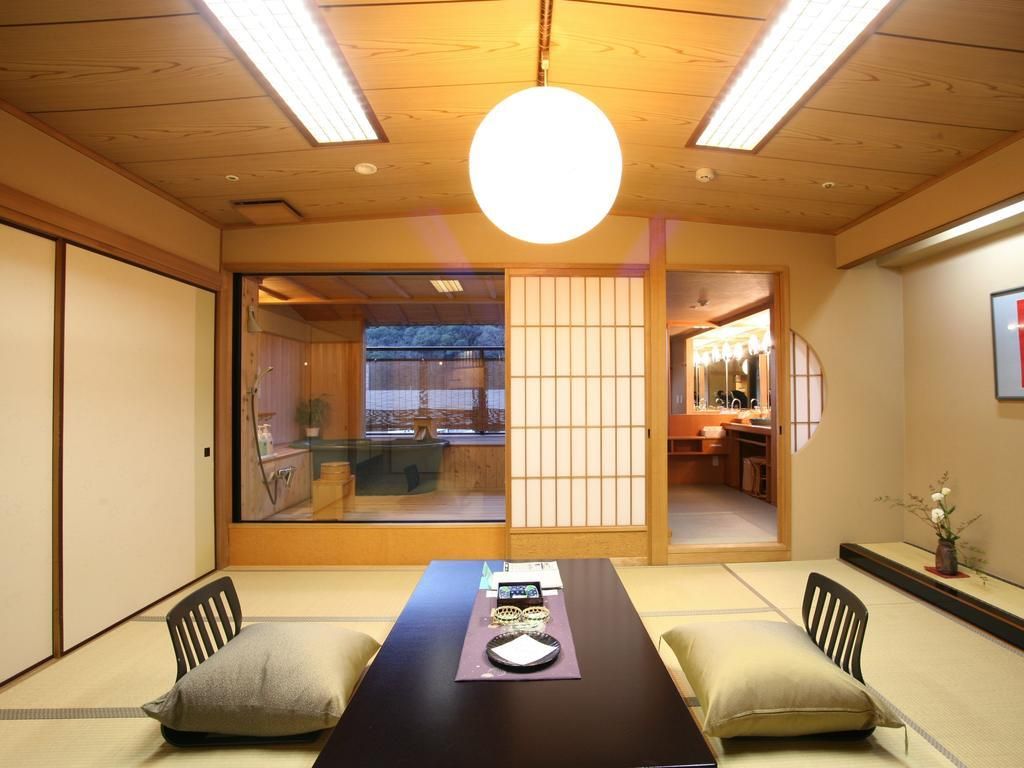 A traditional Japanese room with tatami flooring, a low table with cushions, sliding doors, and a view of the outside.